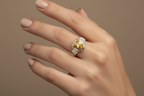 Hand wearing a ring with a yellow gemstone on a neutral background