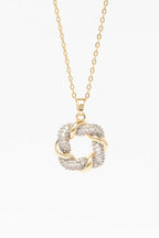 Close-up of champagne gold diamond knot pendant necklace on model showing intricate knot design with pavé crystal detailing, delicate thin chain, polished metallic finish against natural skin tones with soft lighting