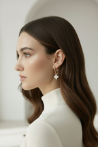 Woman with long brown hair wearing a white turtleneck and star-shaped earrings against a neutral background