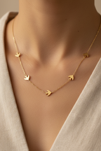 Gold necklace with bird pendants on a person wearing a beige top.