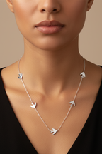 Silver necklace with bird pendants worn by a model against a neutral background