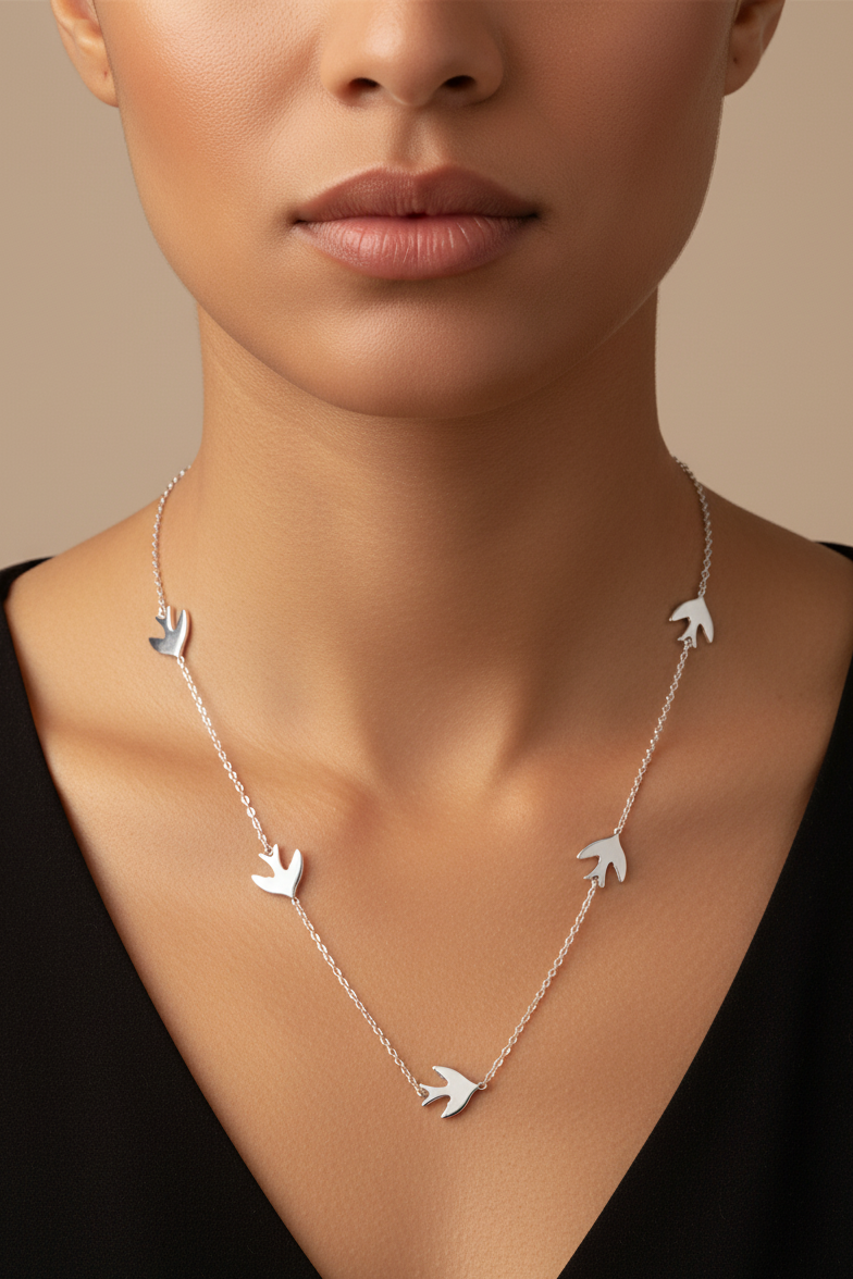 Silver necklace with bird pendants worn by a model against a neutral background