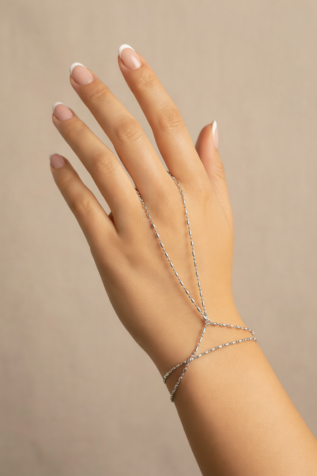 Hand wearing a delicate silver bracelet on a beige background