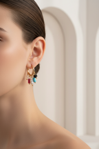 Close-up of a woman wearing a delicate earring with colorful gemstones against a neutral background