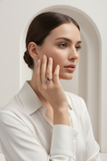  Delicate champagne gold ring with red gemstone centre and pavé crystal halo on hand against neutral beige background, minimal elegant design with polished metallic finish and warm undertones, soft natural lighting