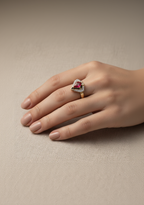 Red stone halo ring in champagne gold on hand showing red gemstone with delicate crystal halo, minimal elegant design with barely-there band and refined craftsmanship, soft natural lighting with warm undertones