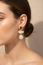 Close-up of a woman wearing gold earrings with pearls against a neutral background
