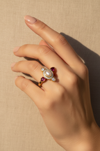 Hand wearing a decorative ring with pearls and gemstones on a beige background
