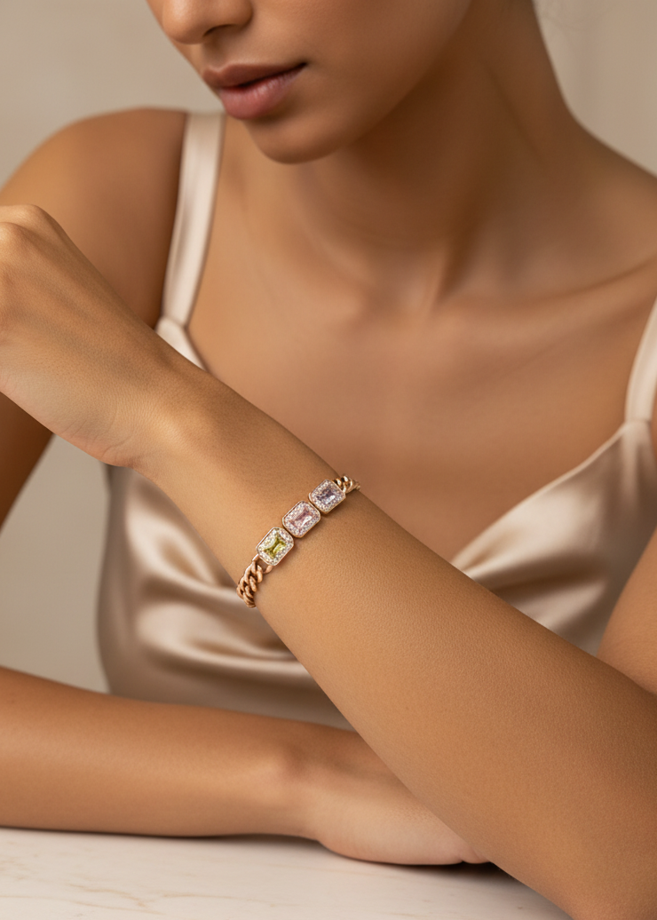 Close-up of a woman's arm wearing a gold bracelet with gemstones on a neutral background