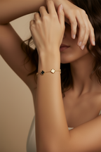 Close-up of a woman's hand wearing a gold bracelet with a green gemstone against a neutral background