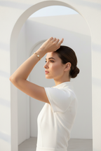 Woman in a white outfit standing in a minimalistic, sunlit space with arches.