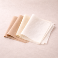 Three folded fabric swatches in beige, cream, and white on a light beige background